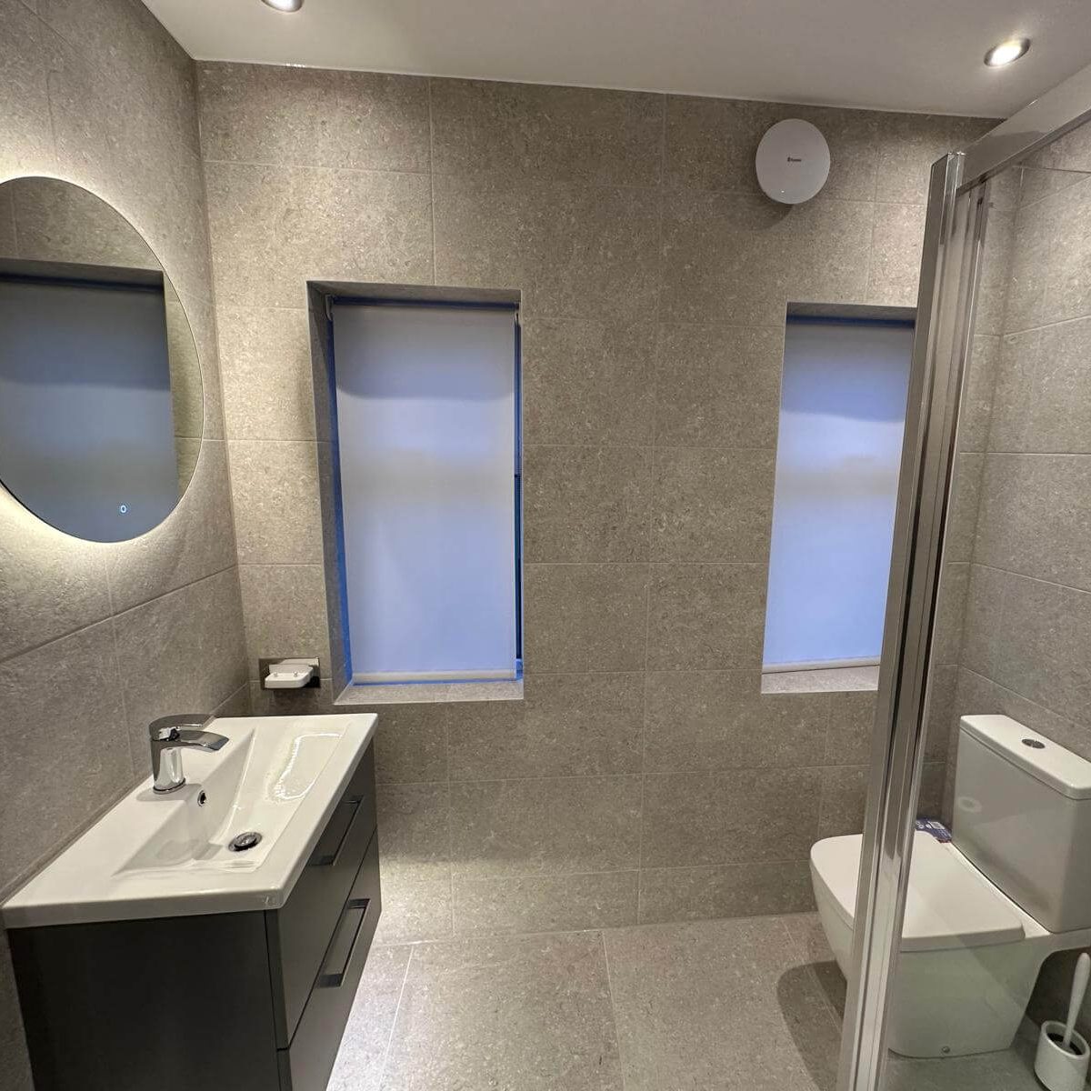 Wall-hung vanity, toilet and shower beside two windows in a renovated Brislington bathroom