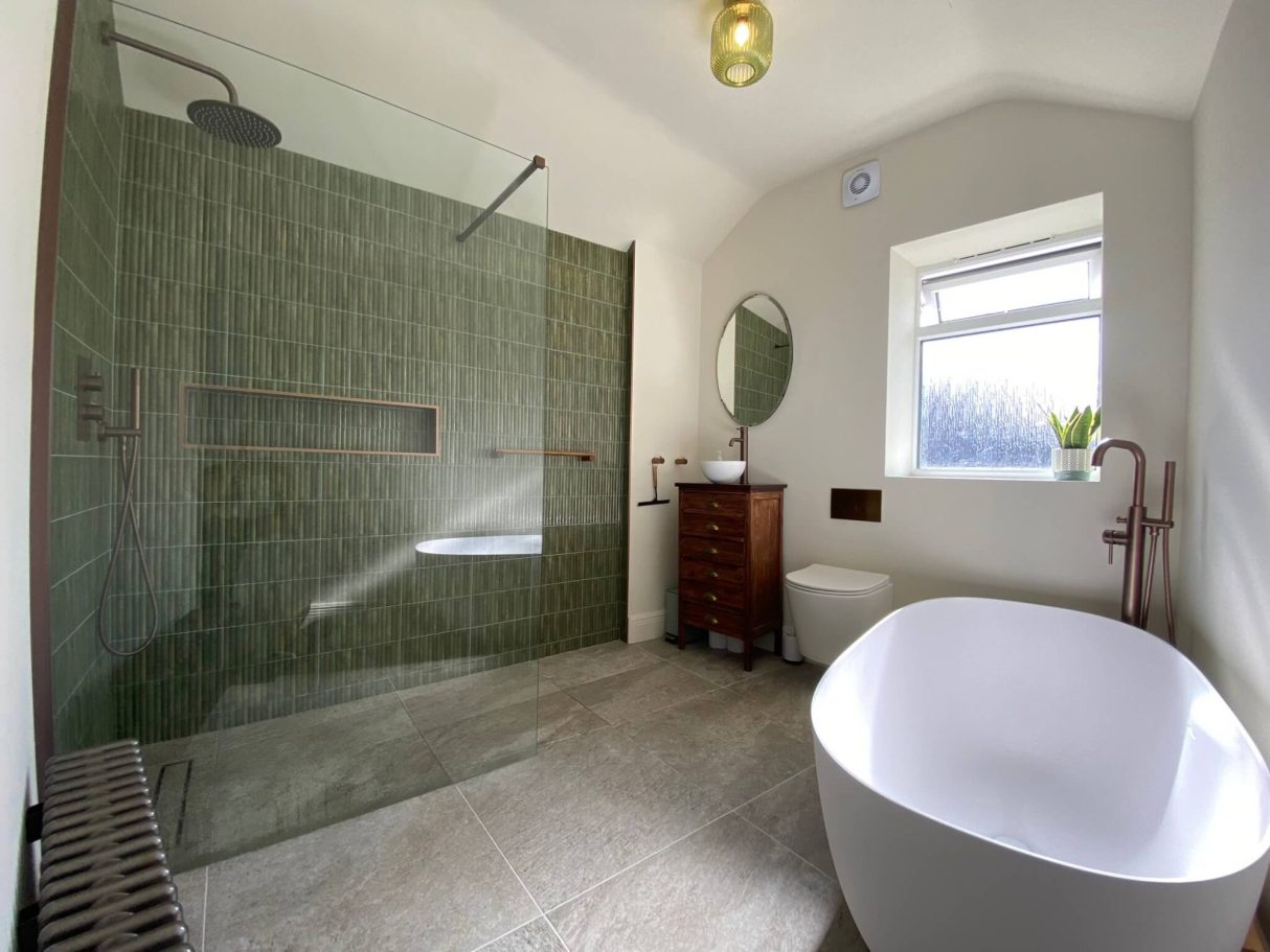 Green tiled walk-in shower beside a wooden vanity and freestanding bath