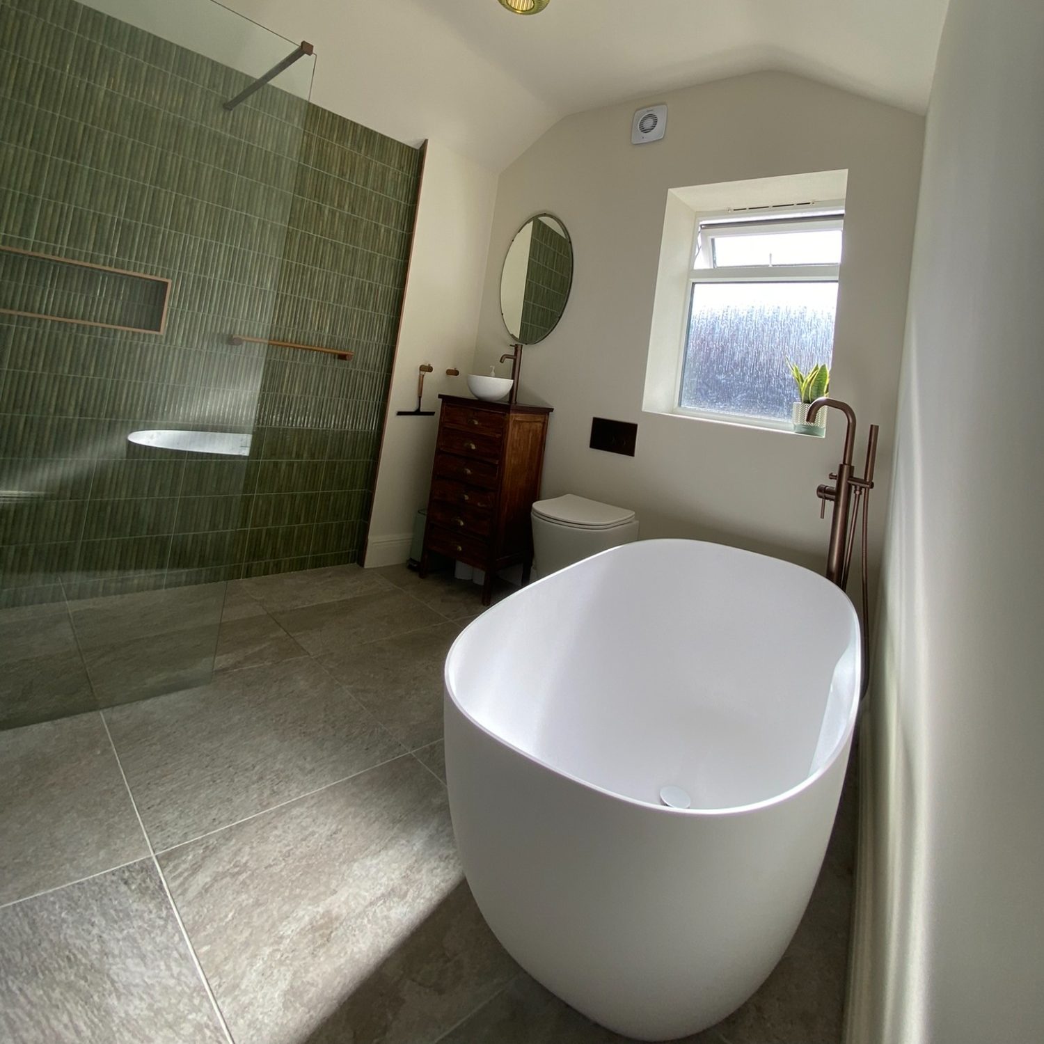 Freestanding white bath beside a green tiled shower in a renovated Southville bathroom