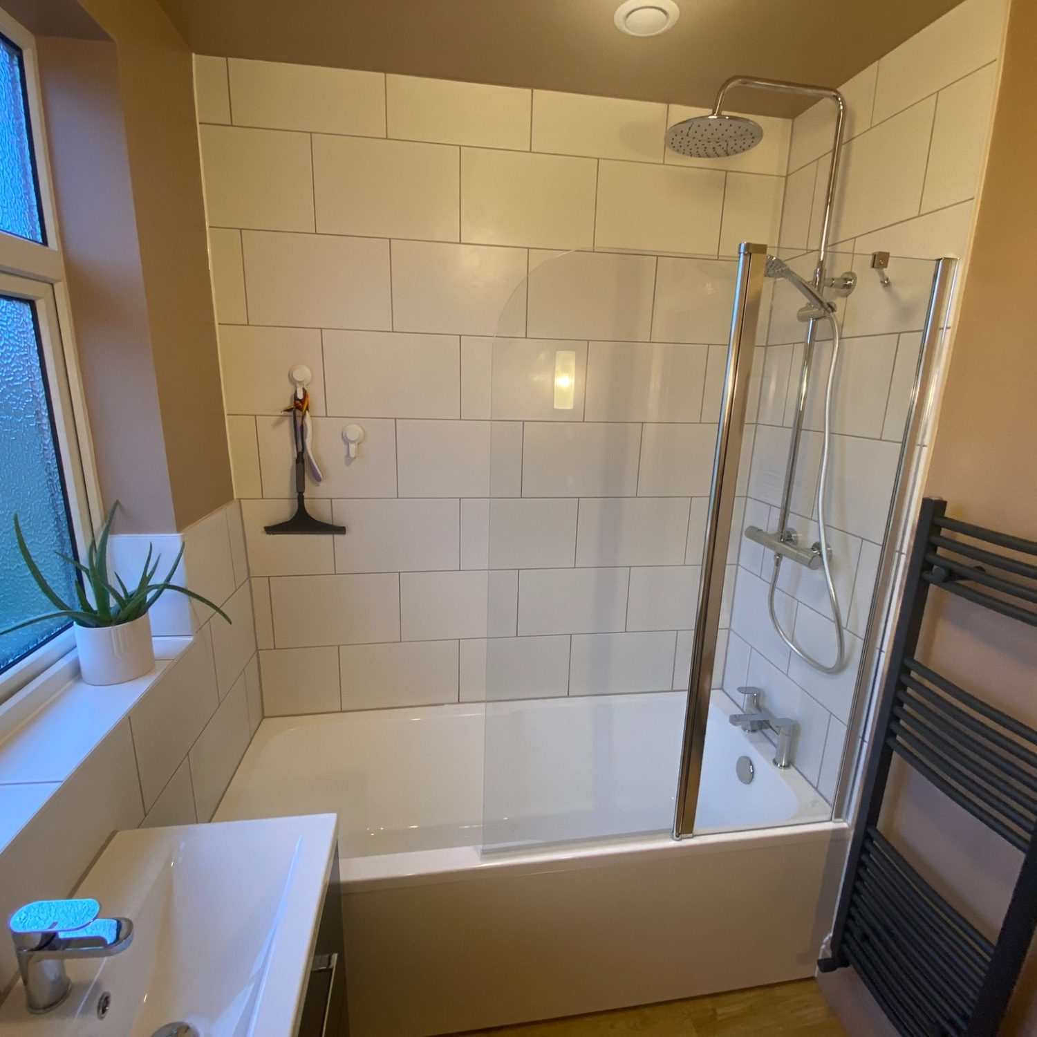 Bath with overhead shower, glass screen and white wall tiles in Brislington