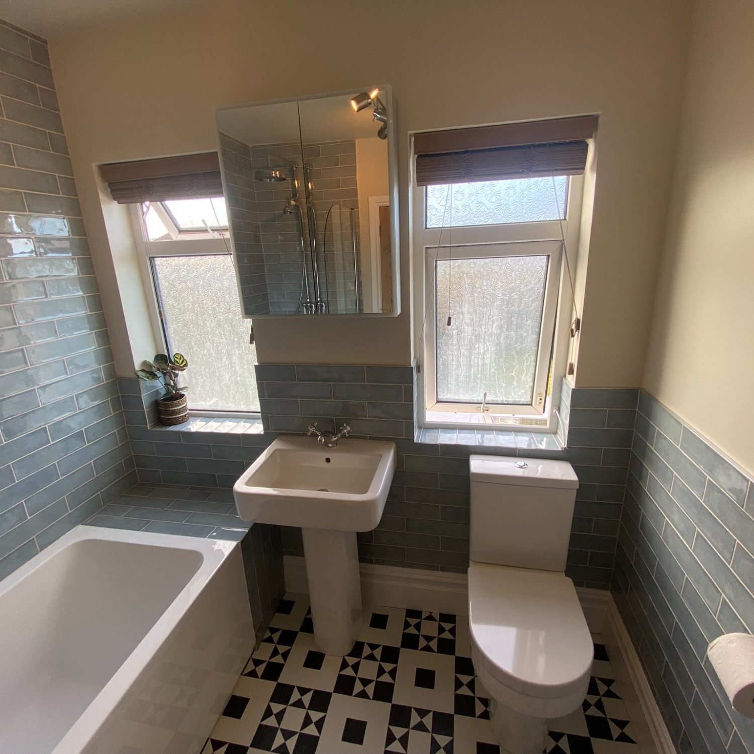 Pedestal basin and toilet beneath a window in a grey tiled Brislington bathroom