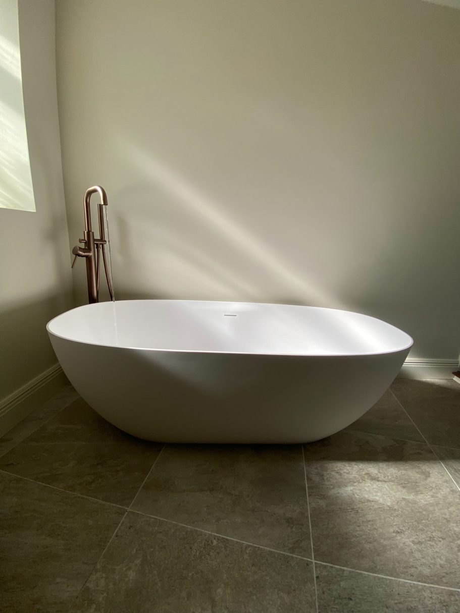 Freestanding white bath beside a window with stone-effect floor tiles