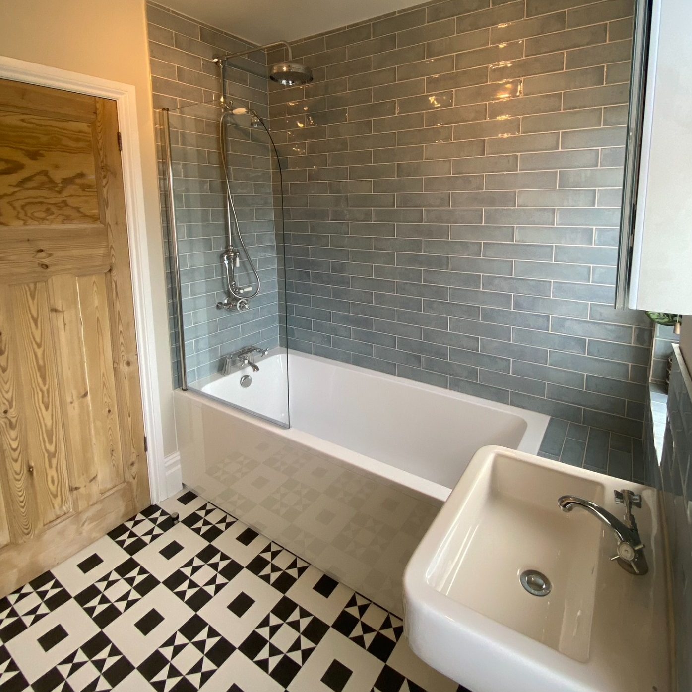 Bath and basin with grey tiled walls and black-and-white geometric flooring in Brislington