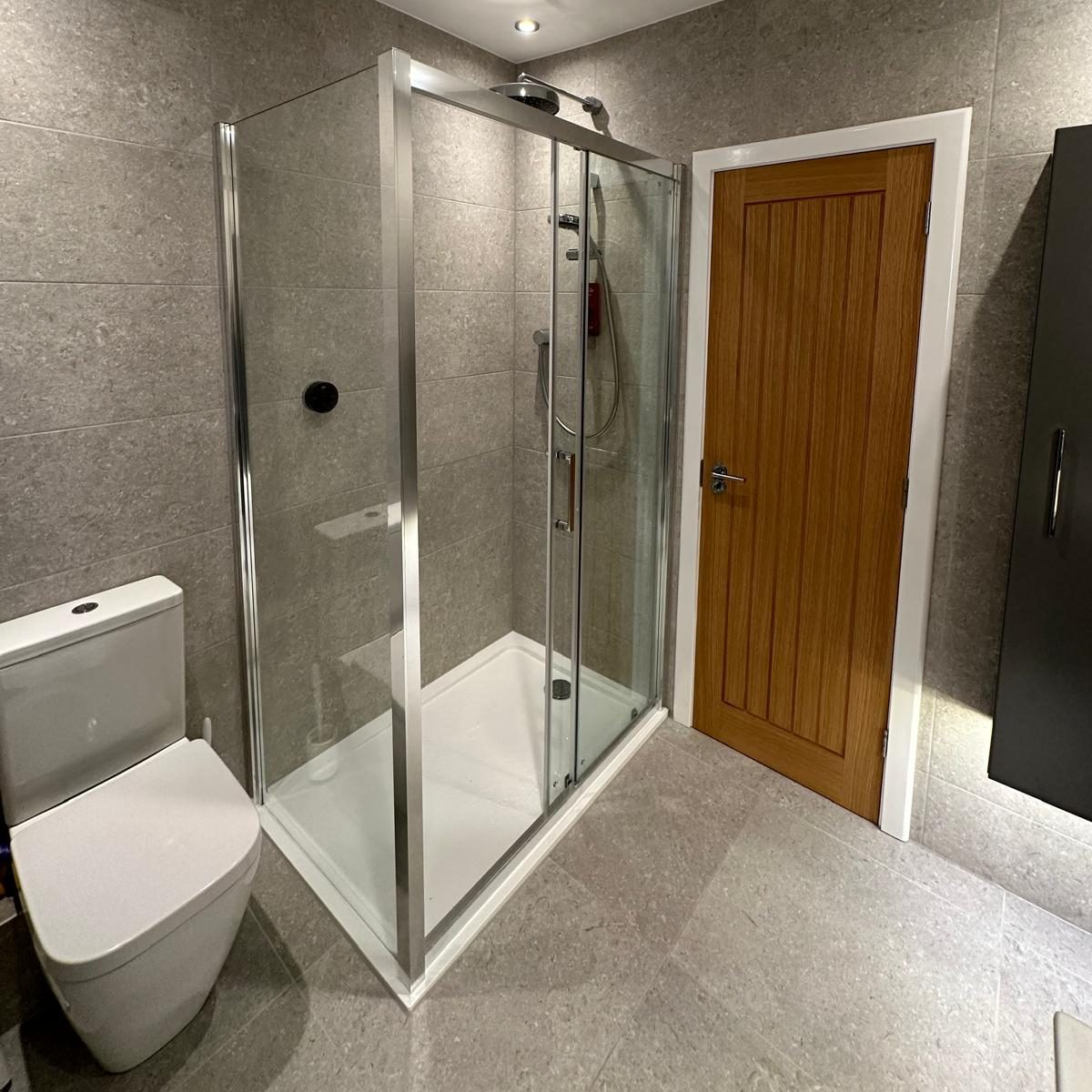 Glass shower enclosure and toilet in a grey tiled Brislington bathroom