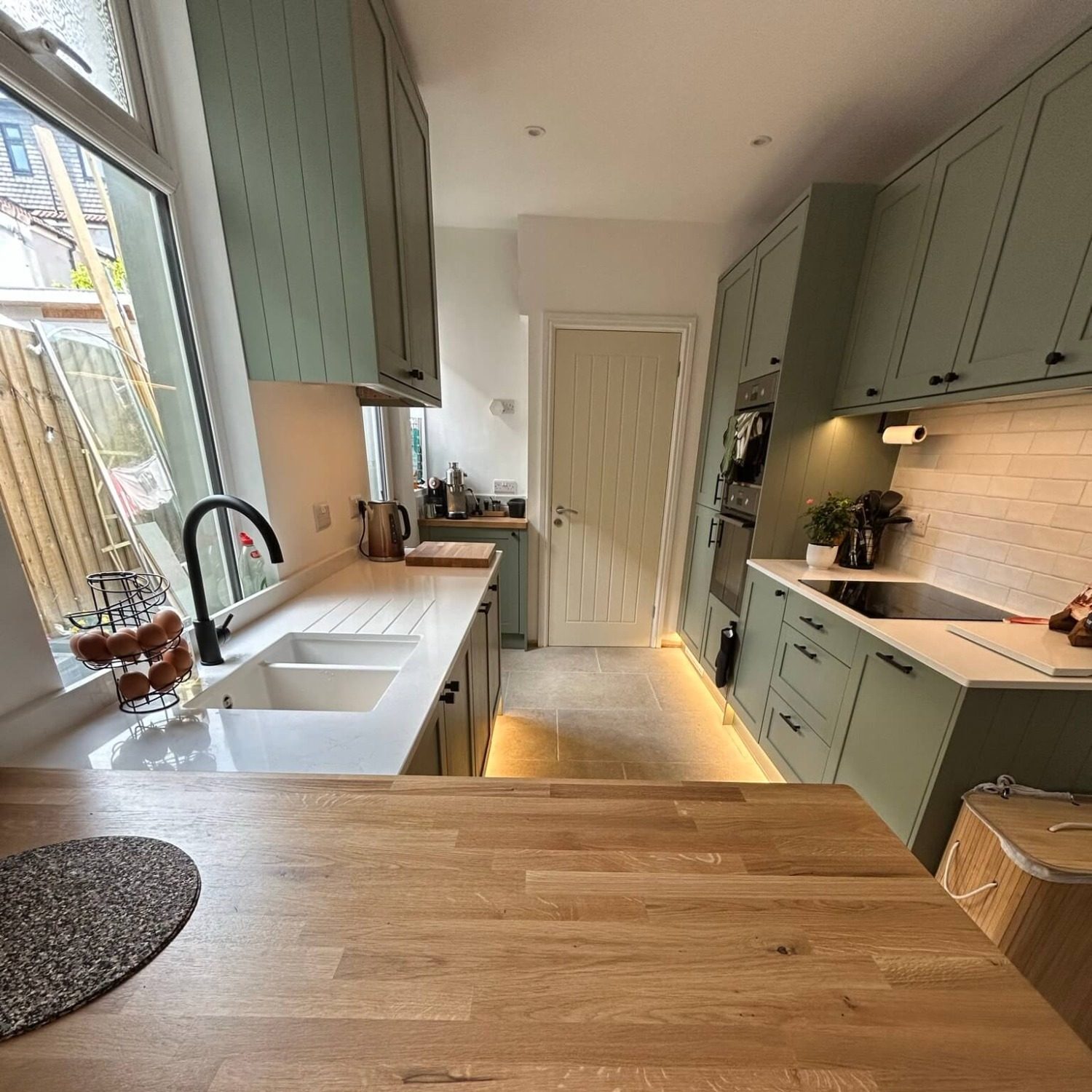 Kitchen sink beneath a window, wooden breakfast bar and green cabinetry in Bedminster