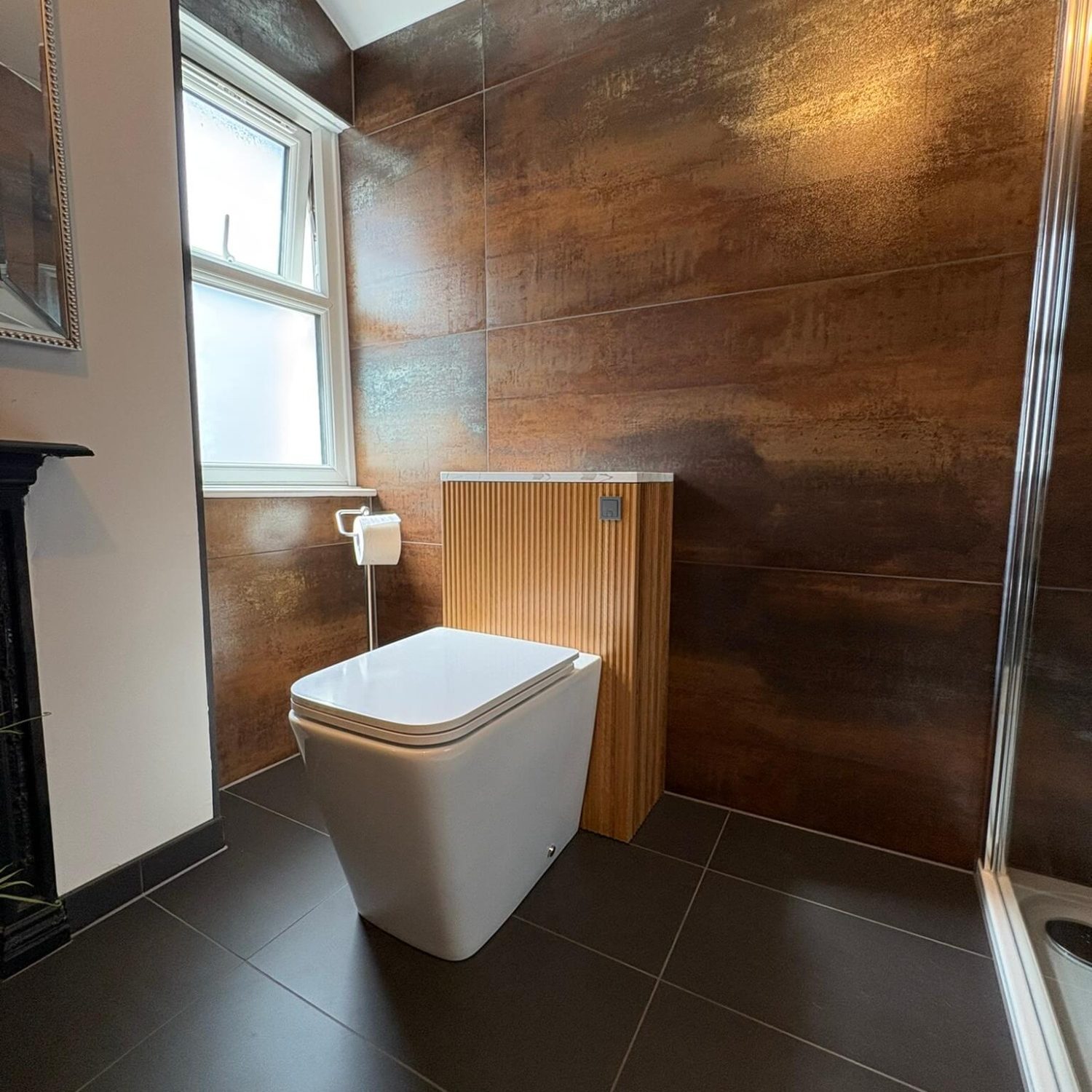 Toilet beside a window and wood-effect tiled wall in a completed Southville bathroom