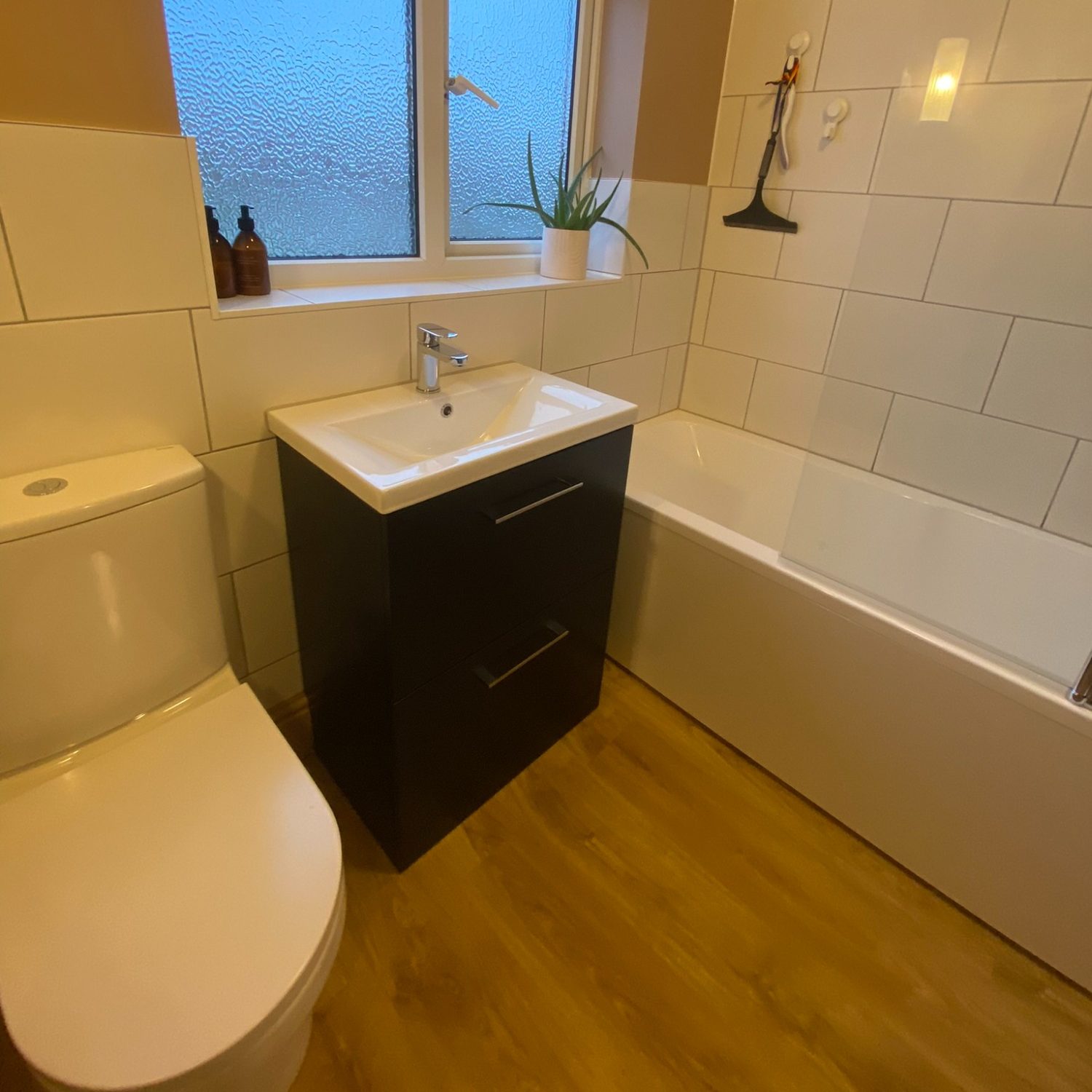 Basin and dark vanity beside a bath with white tiled surround in Brislington