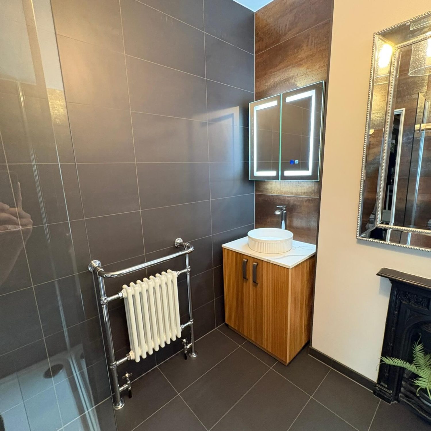 Wooden vanity, illuminated mirror and traditional towel radiator in a tiled Southville bathroom